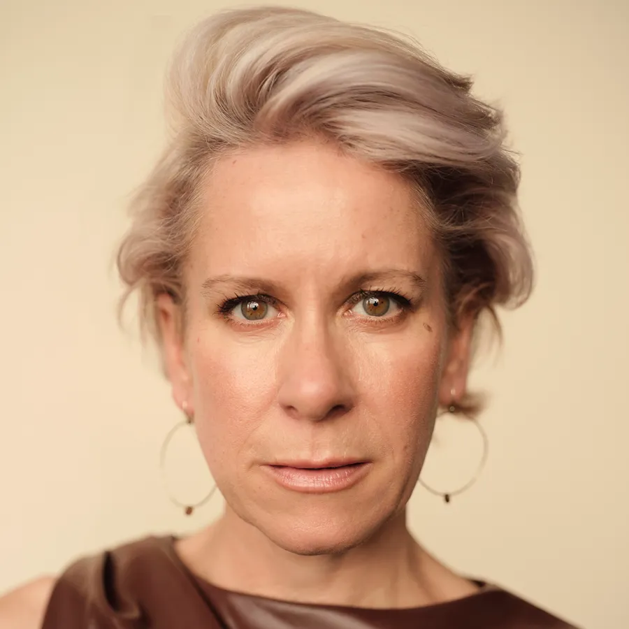 Anna-Jane Casey, cast of One Day the Musical. Headshot with swept-back platinum hair and large hoop earrings.