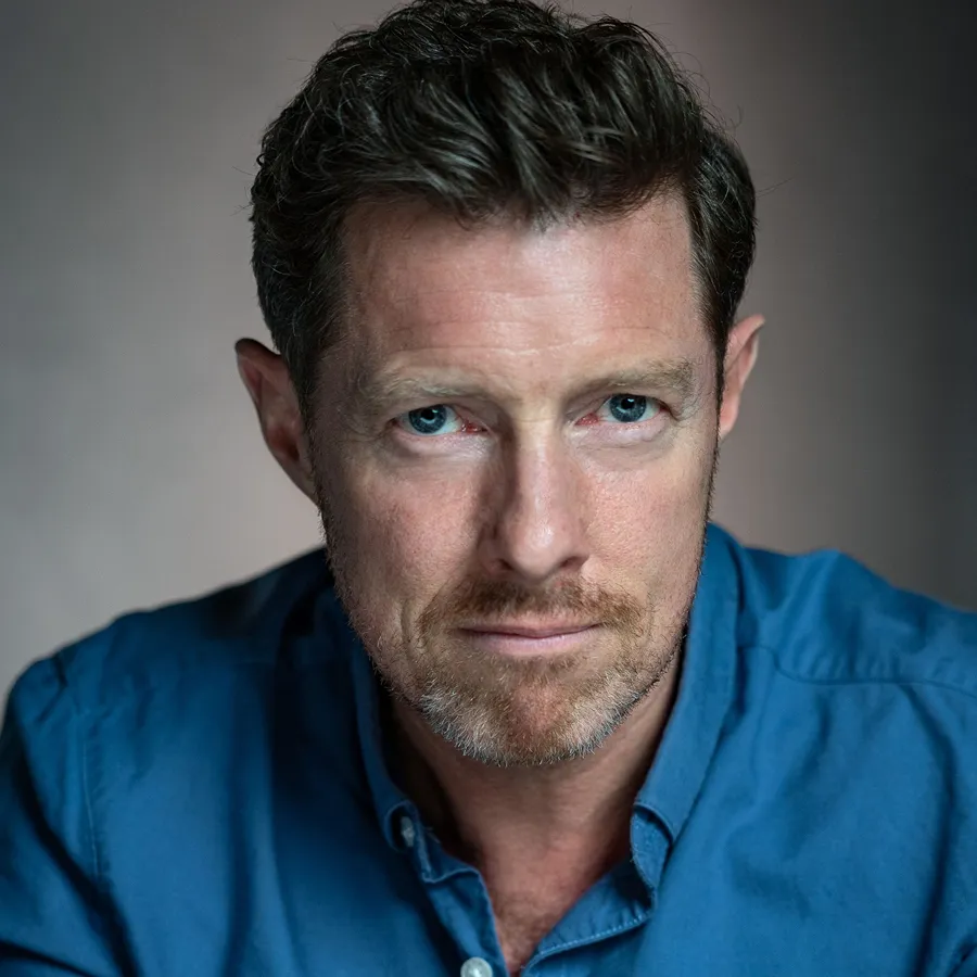 Christopher Dickins, cast of One Day the Musical. Headshot in a blue button-down shirt.