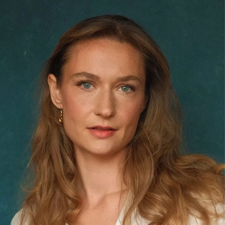 Kelly Hampson, cast of One Day the Musical. Headshot with long hair against a teal backdrop