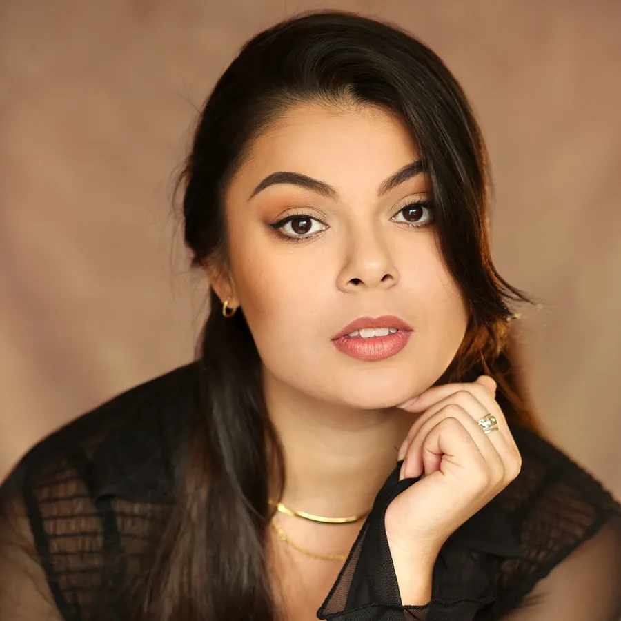 Rosalía Morales, cast of One Day the Musical. Headshot with her hand beneath her chin, wearing gold necklaces.