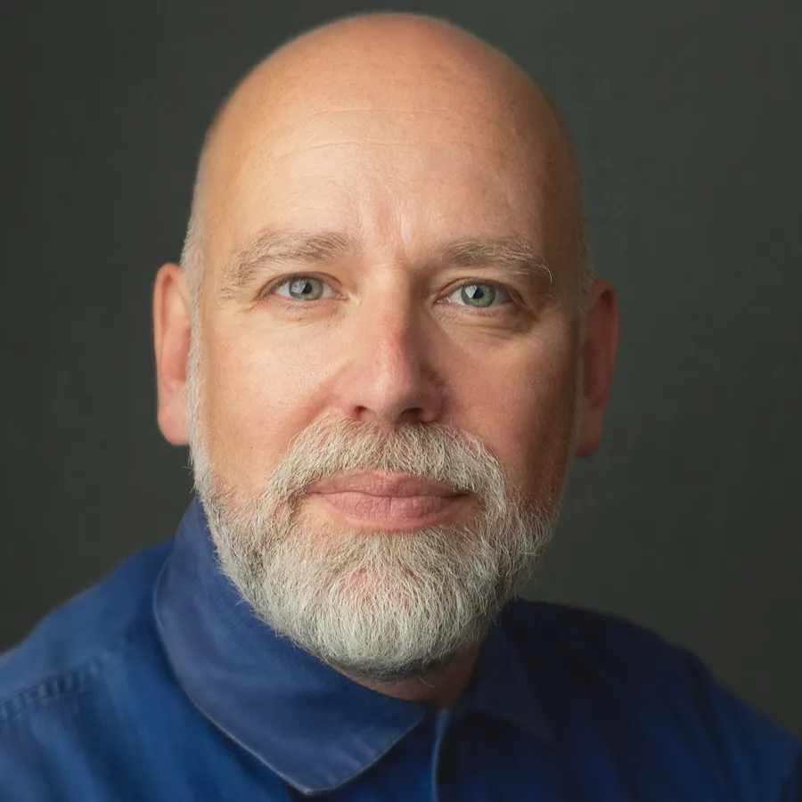 Ross Dawes, cast of One Day the Musical. Headshot with a grey beard, wearing a blue shirt.